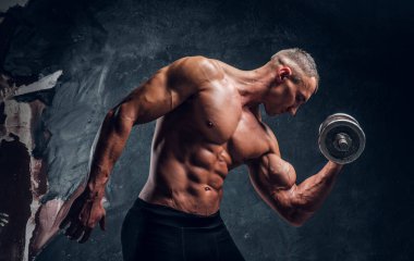 Genç adam bir halterle poz kusursuz pompalanan bir beden ile. Studio fotoğraf karanlık duvar arka plan ile