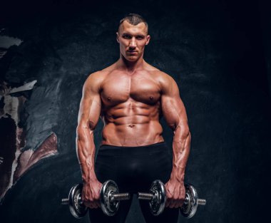 Halter tutan ve bir kameraya bakarak bir kusursuz pompalanan bir beden ile genç bir adam. Studio fotoğraf karanlık duvar arka plan ile