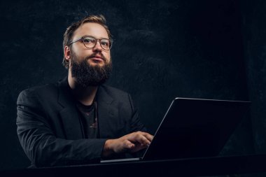 Karanlık bir duvara ofiste dizüstü bilgisayar ile masada oturmuş sakallı bir programcı