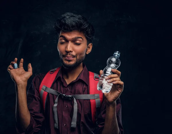 Indiase wandelaar met rugzak kreeg een roeren sensatie dronk een slokje van zoet water. Studio foto tegen een donkere getextureerde muur — Stockfoto