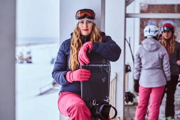 Mulher loira vestindo roupas esportivas de inverno posando com um snowboard — Fotografia de Stock