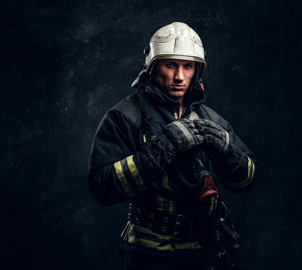 Strażak w mundurze i kask pozowanie w ciemnym studio — Zdjęcie stockowe