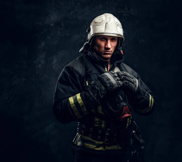 Bombeiro de uniforme e capacete de segurança posando em um estúdio escuro — Fotografia de Stock