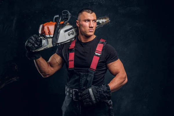 Brutal logger posing with a chainsaw on his shoulder and looks sideways — Stock Photo, Image