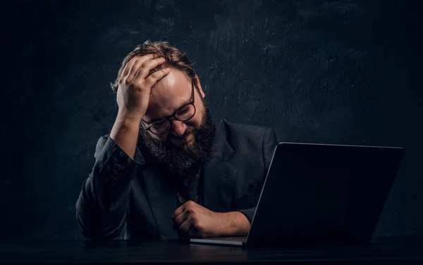 Moe bebaarde programmeur zitten aan de tafel met laptop in kantoor — Stockfoto