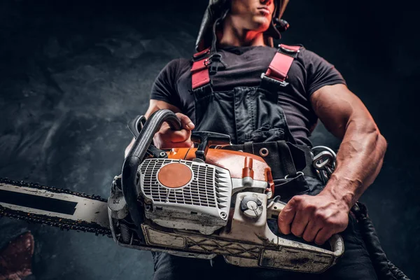 Low angle photo of a lumberjack with a chainsaw in a dark studio — Stock Photo, Image
