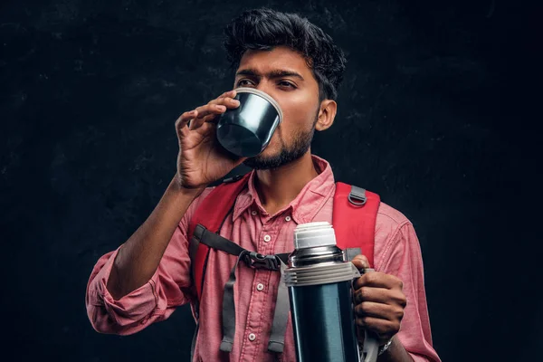Jonge stijlvolle wandelaar met rugzak een thee drinken uit een thermos. — Stockfoto