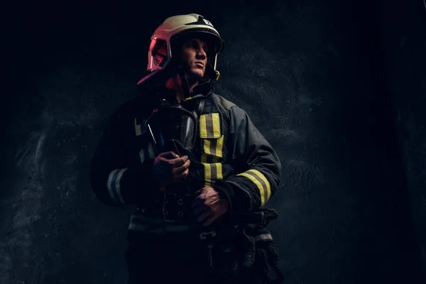 Brutální hasič v uniformě a ochrannou přílbu držení kyslíkovou masku a pohled z boku s jistý pohled. — Stock fotografie