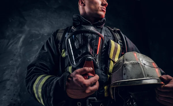 Nízký úhel fotografie muže oblek ohně drží kyslíkovou masku a přilbu, pohled z boku. — Stock fotografie