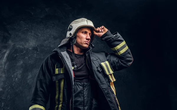 Bombero valiente en un traje de fuego mirando hacia los lados y corrigiendo el casco con su mano — Foto de Stock