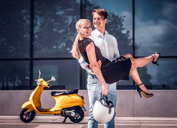 Gelukkige paar verliefd, Guy houden van een meisje op zijn handen staande op een wolkenkrabber in het centrum van de stad op een hete zomerdag — Stockfoto