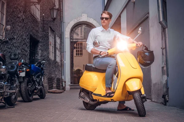 Bonito homem usando óculos de sol montando em scooter italiano vintage na antiga rua estreita da Europa — Fotografia de Stock