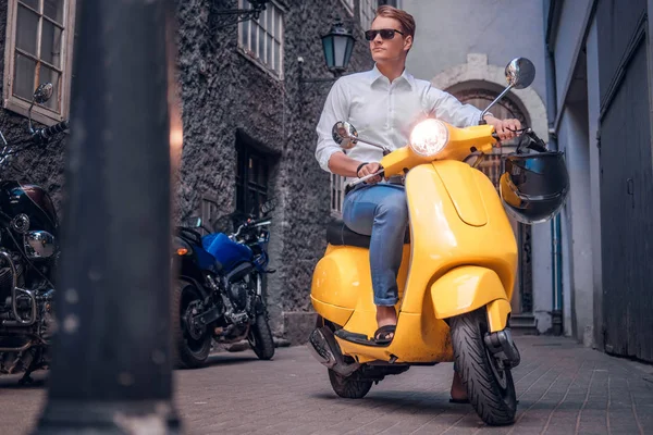 在欧洲古老狭窄的街道上, 戴着太阳镜的帅哥骑着老式的意大利摩托车 — 图库照片