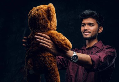 Hintli adam şık gömlek onun sevimli ayıcık elinde tutarken benziyor. Studio fotoğraf bir karanlık dokulu duvara