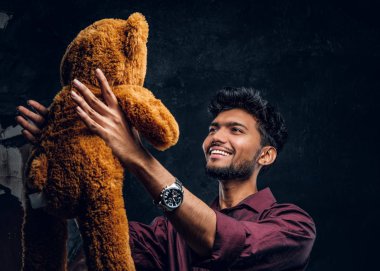 Hintli adam şık gömlek onun sevimli ayıcık elinde tutarken benziyor. Studio fotoğraf bir karanlık dokulu duvara