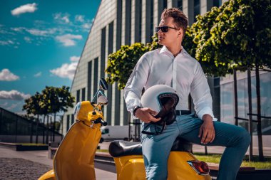 Şık adam bir scooter üzerinde oturan ve yan sokakta güneşli bir günde seyir güneş gözlüğü takıyor