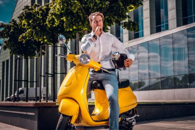 Şık giyimli bir scooter Street üzerinde otururken dalgın bakmak ile poz genç adam