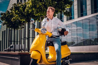 Şık giyimli bir scooter Street üzerinde otururken dalgın bakmak ile poz genç adam