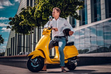 Bir scooter üzerinde oturan ve yan sokakta güneşli bir günde seyir yakışıklı adam