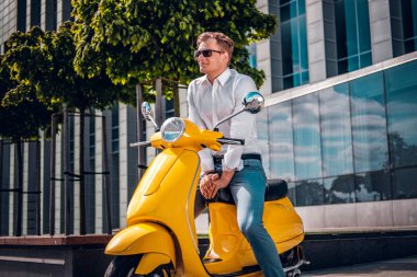 Bir scooter üzerinde oturan ve yan sokağın seyir mutlu yakışıklı adam