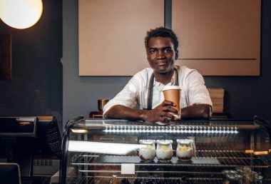 Afrika barista kahve kahve dükkanında tezgahın üzerine eğilerek tutar ve kameraya benziyor