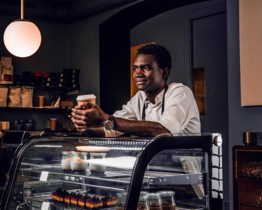 Afrika barista kahve kahve dükkanında tezgahın üzerine eğilerek tutar ve kameraya benziyor