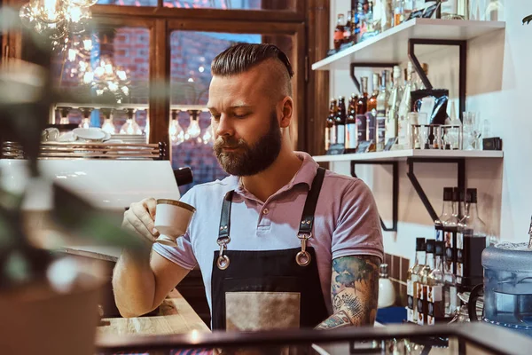 Barista en delantal tomando café durante la pausa para el almuerzo de pie detrás del mostrador en la cafetería —  Fotos de Stock