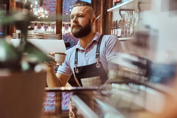 Barista v zástěře pití kávy během polední přestávky, stojící za pultem v kavárně — Stock fotografie