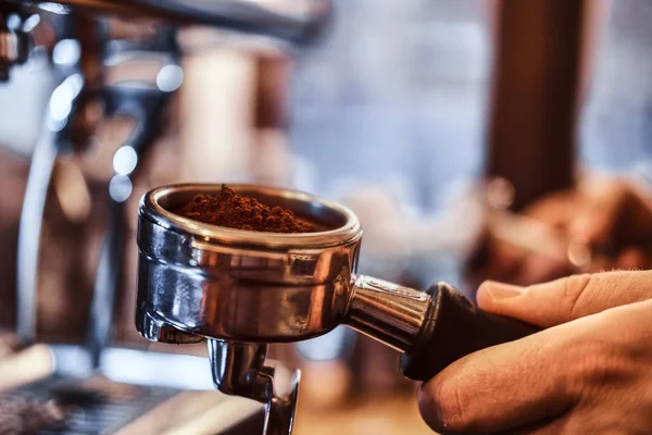 Foto de close-up de uma mão segurando um portafilter com um café moído preto em uma cafeteria ou restaurante — Fotografia de Stock