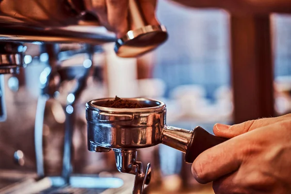 Close-up photo ręki trzymającej ubijaka czarną mieloną kawę w kawiarni sklepu lub restauracji — Zdjęcie stockowe