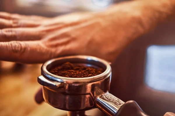 Nahaufnahme einer Hand, die einen Portafilter mit schwarzem gemahlenem Kaffee in einem Café oder Restaurant hält — Stockfoto