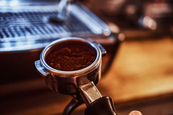 Close-up photo of a hand holding a portafilter with a black ground coffee in a cafe shop or restaurant — Stock Photo, Image