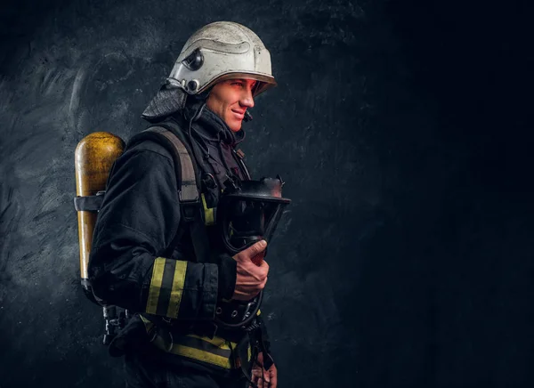 Brandman i full skyddsutrustning håller en syrgasmask och tittar på en kamera. — Stockfoto