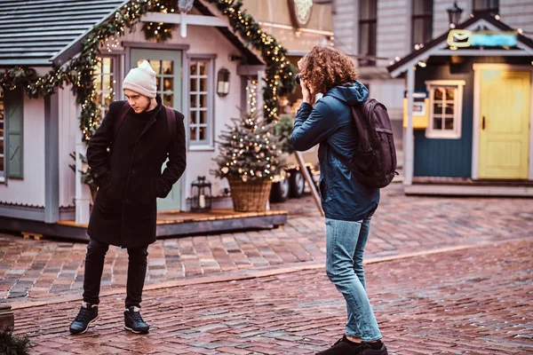 Junger lockiger Fotograf mit Rucksack macht ein Foto von einem Freund — Stockfoto