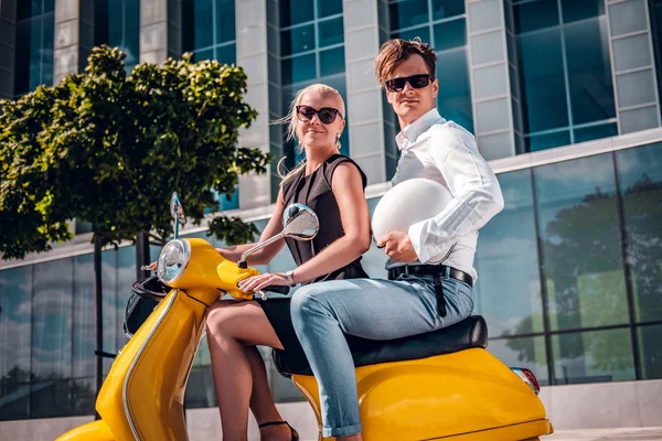Romantische paar zittend op een klassieke Italiaanse scooter op de straat van een moderne deel van een Europese stad — Stockfoto