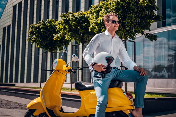 Elegante tipo con gafas de sol sentado en una scooter y mirando de lado en la calle en un día soleado —  Fotos de Stock