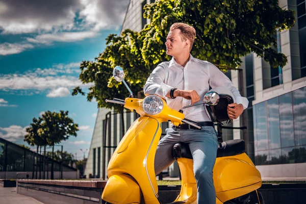 Hombre guapo sentado en un scooter y mirando hacia los lados en la calle en un día soleado —  Fotos de Stock