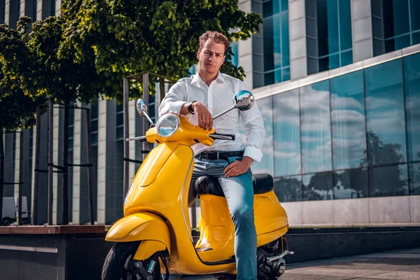 Hombre guapo con una mirada segura sentado en un scooter y mirando una cámara en la calle — Foto de Stock