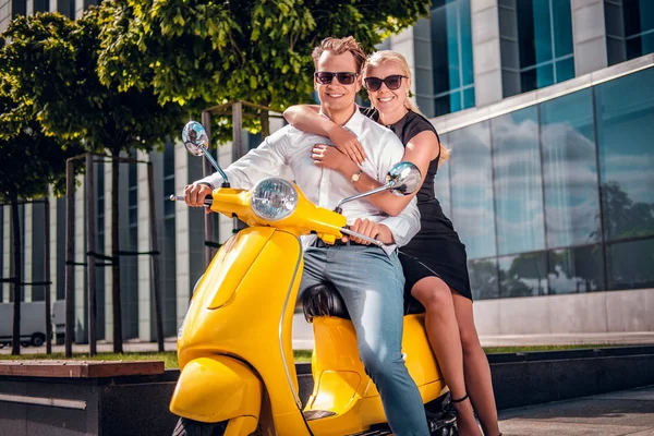 Romantische paar zittend op een klassieke Italiaanse scooter op de straat van een moderne deel van een Europese stad — Stockfoto