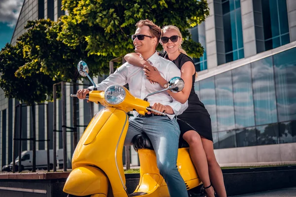 Romantische paar zittend op een klassieke Italiaanse scooter op de straat van een moderne deel van een Europese stad — Stockfoto