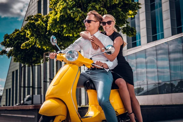 Casal romântico sentado em uma scooter italiana clássica na rua de uma parte moderna de uma cidade europeia — Fotografia de Stock