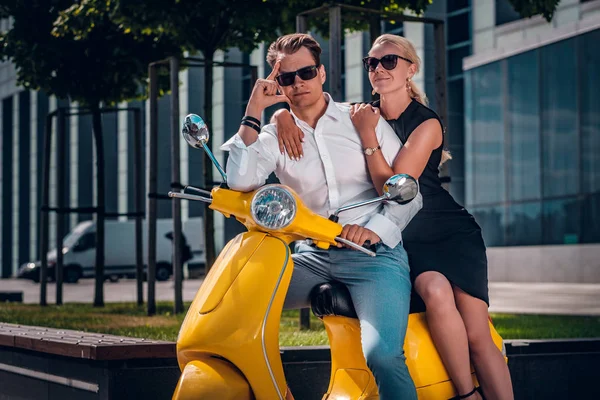 Romantic couple sitting on a classic Italian scooter on the street of a modern part of a European city — Stock Photo, Image