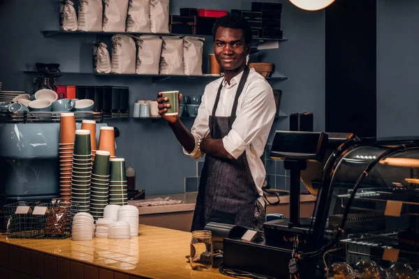 Afrika barista süre arkasında, bir kafede bir sayacı ve bir kameraya bakarak bir fincan kahve ile tutarak  