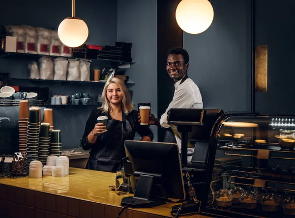 Dos baristas multirraciales sosteniendo un café mientras están de pie detrás de un mostrador en una cafetería o cafetería —  Fotos de Stock