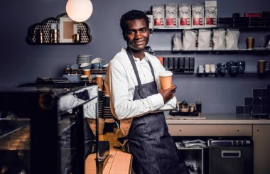 Bir fincan kahve ile bir kafede bir sayaçta yaslanmış ve bir kameraya bakarak süre tutarak Barista