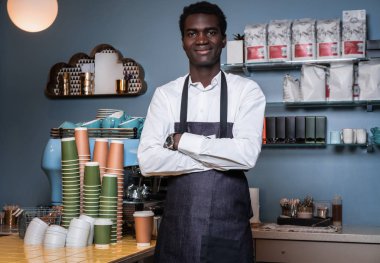 Barista ayakta kolları geçti ve bir kamera bir kafede bakarak