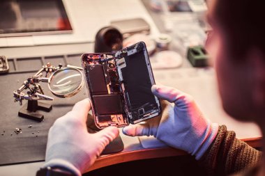 Teknisyen dikkatle smartphone içinde modern bir tamirciye iç unsurları bütünlüğünü inceler