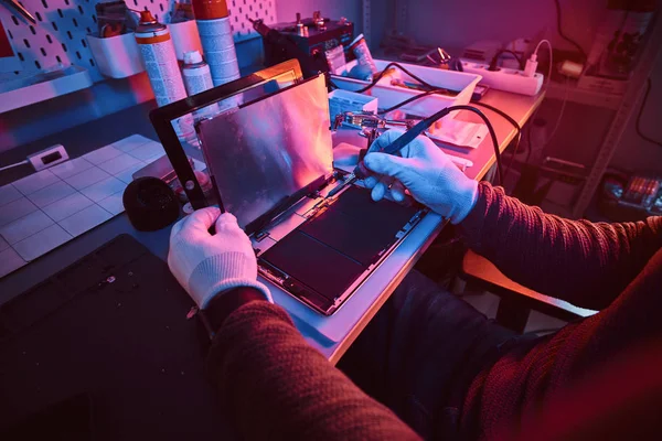 Der Techniker repariert einen kaputten Tablet-Computer in einer Werkstatt. Beleuchtung mit rotem und blauem Licht — Stockfoto