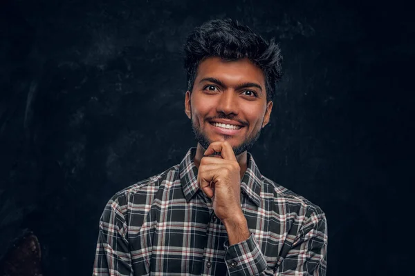 Handsome Indian guy in plaid shirt smiling and looks at the camera with a piercing look.