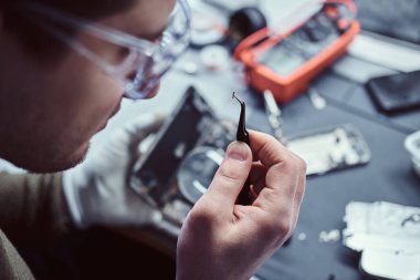 Elektronik teknisyeni kırık bir telefon tamir cımbızla tutan küçük cıvata yakından bakarak